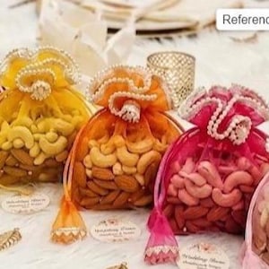 Puede incluir: Una variedad de bolsas de cordón coloridas llenas de nueces. Las bolsas son en tonos de rojo, amarillo, naranja, rosa y rosa claro. Cada bolsa está adornada con adornos y perlas decorativas, y llena de anacardos y almendras.