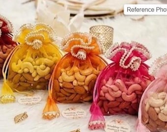May include: An assortment of colorful, sheer drawstring bags filled with nuts. The bags are in shades of red, yellow, orange, pink, and light pink. Each bag is adorned with decorative trim and pearls, and filled with cashews and almonds.