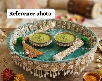 May include: A decorative teal tray with a beaded and pearl trim, holding two small silver bowls filled with green powder. A beaded item and a tassel are also on the tray. The text "Reference photo" is in the image.