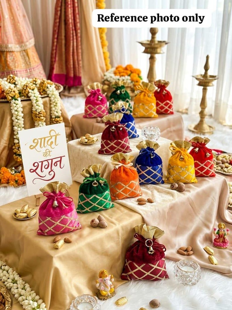 May include: A collection of colorful velvet gift bags with gold accents and diamond patterns. The bags are arranged on a table with almonds and small decorative figurines. The image includes a sign with text in a foreign language.