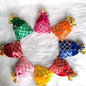 May include: A collection of colorful, small fabric pouches arranged in a circle. Each pouch is a different color, including green, pink, orange, blue, red, and yellow. They have a gold diamond pattern and gold ribbon ties. The text "Jaipurweddingshop" is visible.