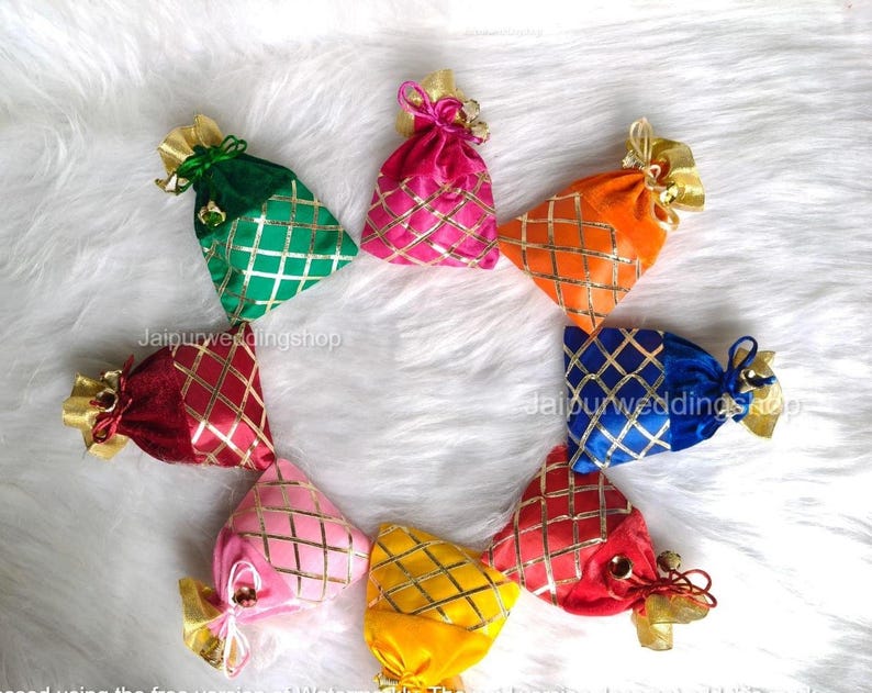 May include: A collection of colorful, small fabric pouches arranged in a circle. Each pouch is a different color, including green, pink, orange, blue, red, and yellow. They have a gold diamond pattern and gold ribbon ties. The text "Jaipurweddingshop" is visible.