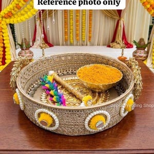 Peut inclure: Un panier rond et tissé avec des bordures dorées, des perles et des accents jaunes. À l'intérieur, un bol doré rempli de poudre jaune, un objet décoratif avec des plumes colorées et un objet doré. Le texte "Reference photo only" est en haut.