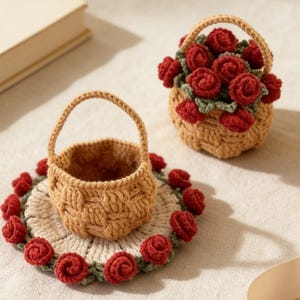 May include: Two miniature crochet baskets. One basket is empty, and the other is filled with red crochet roses and green leaves. The empty basket sits on a round coaster decorated with red roses. The baskets are tan and have arched handles.