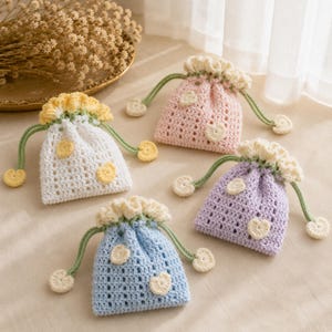 May include: Four small drawstring pouches made of crocheted yarn in white, pink, lavender, and light blue. Each pouch features a ruffled top edge, green drawstring cords with heart-shaped ends, and small heart-shaped appliqués on the front.
