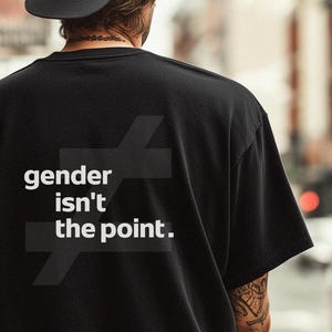 Könnte beinhalten: Schwarzes T-Shirt mit dem weißen Text "gender isn't the point.". Das Design ist minimalistisch, mit einer klaren Botschaft. Das Bild zeigt die Rückseite des T-Shirts, wobei der Text deutlich sichtbar ist.