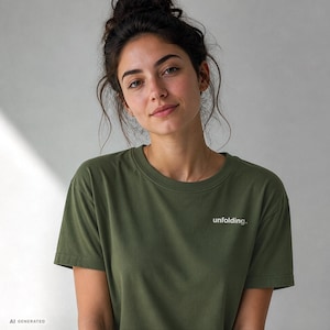 May include: An olive green short-sleeved t-shirt featuring the word unfolding. printed in small white lowercase letters on the left side of the chest. The garment has a classic crew neckline and a simple, clean design with short sleeves.
