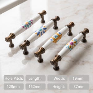 May include: Four cabinet pulls with white ceramic centers and antique brass metal ends. Each pull features a unique colorful floral pattern. Dimensions include a 128mm hole pitch, 152mm length, 19mm width, and 37mm height as specified in the image text.