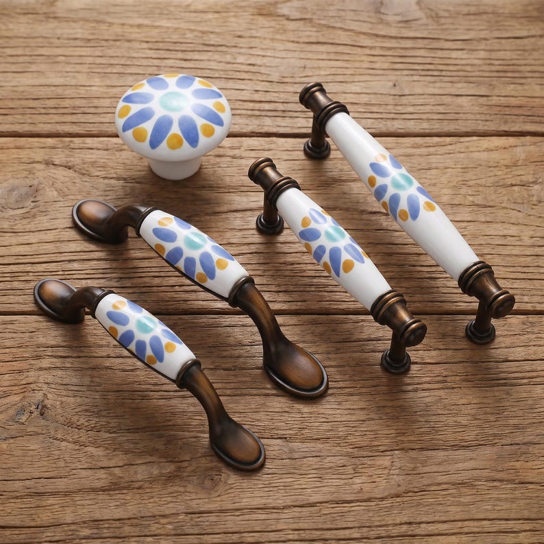 May include: A collection of cabinet hardware including one round ceramic knob and three arched metal drawer pulls. Each piece features a white ceramic base decorated with a repeating pattern of blue and yellow petals around a central light blue dot.
