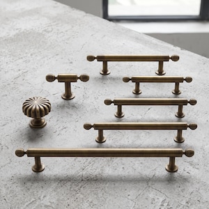 May include: A collection of antique brass cabinet hardware including one round fluted knob and five bar pulls of varying lengths. Each pull features a cylindrical rod with a small ribbed sphere at both ends and two circular mounting posts.