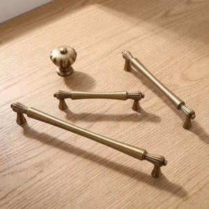 May include: A set of antique brass hardware including one round fluted knob and three linear drawer pulls of varying lengths. Each piece features a smooth cylindrical bar design with decorative fluted detailing at the ends and mounting posts.