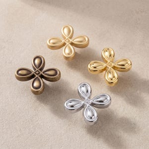 May include: Four metal cabinet knobs arranged in a cluster, each featuring a four-petaled flower shape with a central square detail. The set includes one matte gold, one polished gold, one antique bronze, and one polished silver finish knob.