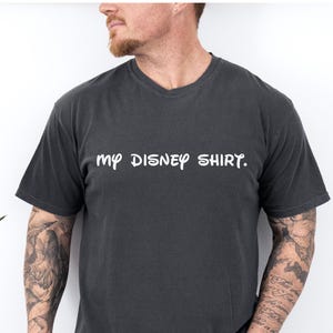 May include: Dark gray t-shirt with the text "my DISNEY SHIRT." in white, casual font. The shirt has short sleeves and a crew neck. The shirt is made of a soft material.