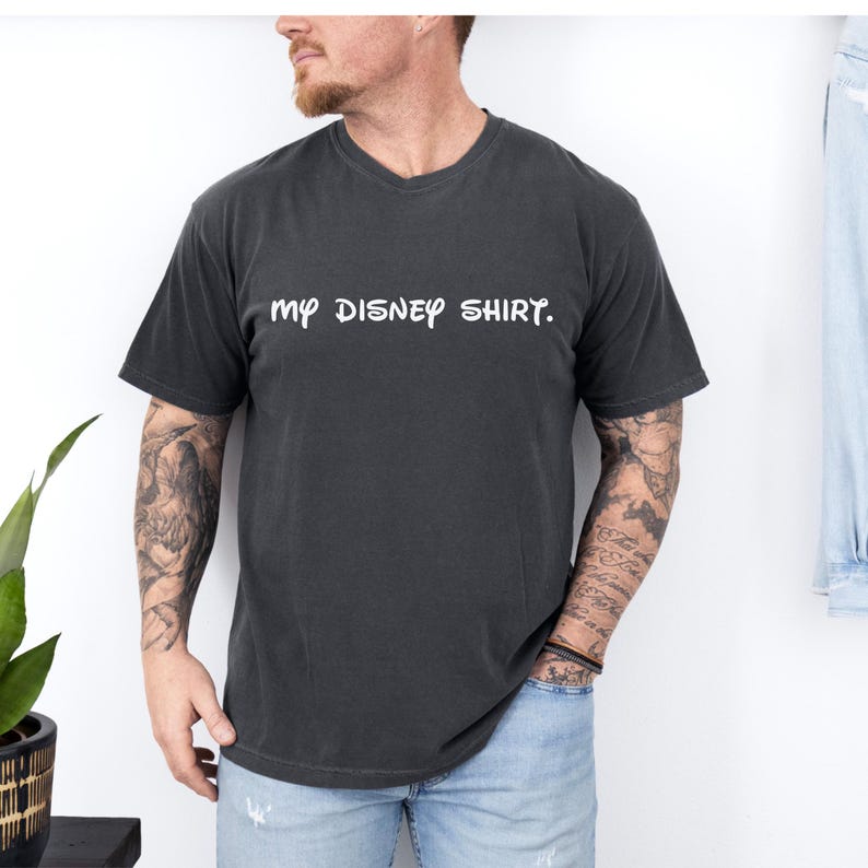 May include: Dark gray t-shirt with the text "my DISNEY SHIRT." in white, casual font. The shirt has short sleeves and a crew neck. The shirt is made of a soft material.