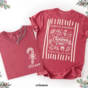 May include: A crimson red t-shirt featuring a white graphic of a candy cane and the name Oliver on the front. The back displays a white graphic with the text Smith Family, Christmas Crew, and Charleston, SC 2026, surrounded by holiday icons.