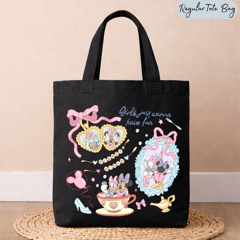 May include: A black tote bag featuring a graphic print of Disney characters Daisy Duck and Minnie Mouse. The design includes a heart-shaped locket, a mirror, a teacup, a golden lamp, and the text "Girls just wanna have fun" and "Disney Girls".