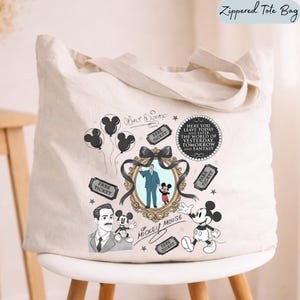 May include: A cream-colored canvas tote bag featuring a black and gold graphic print. The design includes illustrations of Mickey Mouse, Walt Disney, park tickets, balloons, and a circular plaque with the text Here You Leave Today And Enter The World Of Yesterday, Tomorrow And Fantasy.
