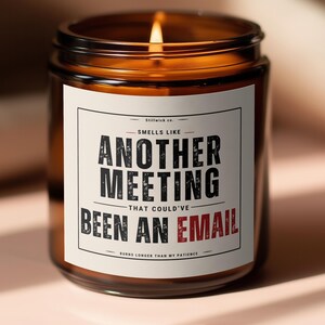 Peut inclure: Un pot de bougie en verre brun allumé avec une étiquette blanche. L'étiquette indique « Smells Like Another Meeting That Could've Been An Email ». La flamme de la bougie est vive. Le fond est rose clair.