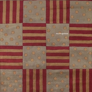 Könnte beinhalten: Ein gemusterter Teppich mit Schachbrettmuster. Der Teppich hat abwechselnd Quadrate in Grau mit tanfarbenen Punkten, roten Streifen und tanfarbenen Streifen. Das Design des Teppichs ist symmetrisch und geometrisch.