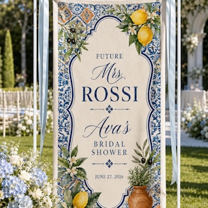 May include: A vertical fabric banner featuring a blue and orange tile pattern border, yellow lemons, green olive branches, and a brown terracotta vase. The text reads: FUTURE Mrs. ROSSI Ava's BRIDAL SHOWER JUNE 27, 2026, centered on a cream background.