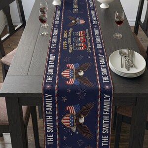 May include: A navy blue table runner with a patriotic design. It features an American flag and eagle graphic, with text that reads "1776-2026 Happy 250th Birthday" and "USA 250 years of freedom". The runner is decorated with stars and fireworks.