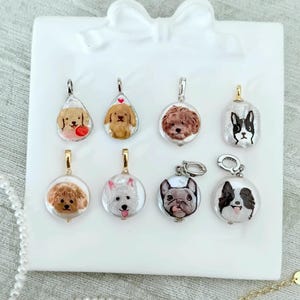 以下が含まれることがあります： 犬をテーマにした8つのペンダントのコレクション。各ペンダントは、異なる犬種のイラストを透明な楕円形の樹脂にセットしています。ペンダントには、ネックレスやブレスレットに取り付けるための銀色または金色メッキの金属製金具が付いています。