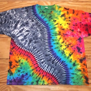 May include: A tie-dye t-shirt with a vibrant rainbow design. The shirt features a diagonal pattern with a mix of colors, including black, red, orange, yellow, green, blue, and purple. The shirt is made of a soft material and has a crew neck.