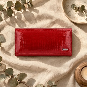 May include: A rectangular red wallet with a glossy, textured finish resembling crocodile skin. The wallet features a small silver-toned metal plaque on the bottom right corner with the brand name HengHuang printed in black text.