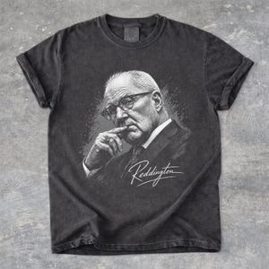 May include: A charcoal grey short-sleeve t-shirt featuring a white graphic illustration of a man wearing glasses and a suit, with his hand near his chin. The word Reddington is written in a white cursive script below the portrait illustration.