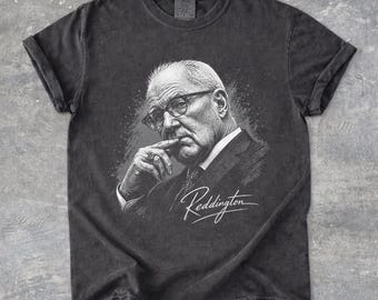 May include: A charcoal grey short-sleeve t-shirt featuring a white graphic illustration of a man wearing glasses and a suit, with his hand near his chin. The word Reddington is written in a white cursive script below the portrait illustration.