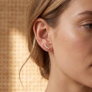May include: A gold ear climber earring featuring a row of four marquise-cut clear stones arranged in a curved, leaf-like pattern that follows the natural shape of the earlobe. The metal has a polished finish and a warm, metallic gold tone.