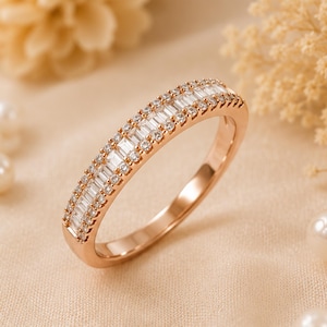 Könnte beinhalten: Ein Ring aus Roségold mit einer zentralen Reihe aus klaren Baguette-Schliff-Steinen, flankiert von zwei äußeren Reihen kleiner, runder, klarer Steine. Das Metall hat eine polierte Oberfläche und ein durchgehendes Funkeln.