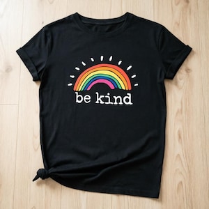 May include: Black t-shirt with a rainbow graphic and the words "be kind" in white. The rainbow design includes red, orange, yellow, green, blue, and purple. The shirt has a crew neck and is made of a soft material.