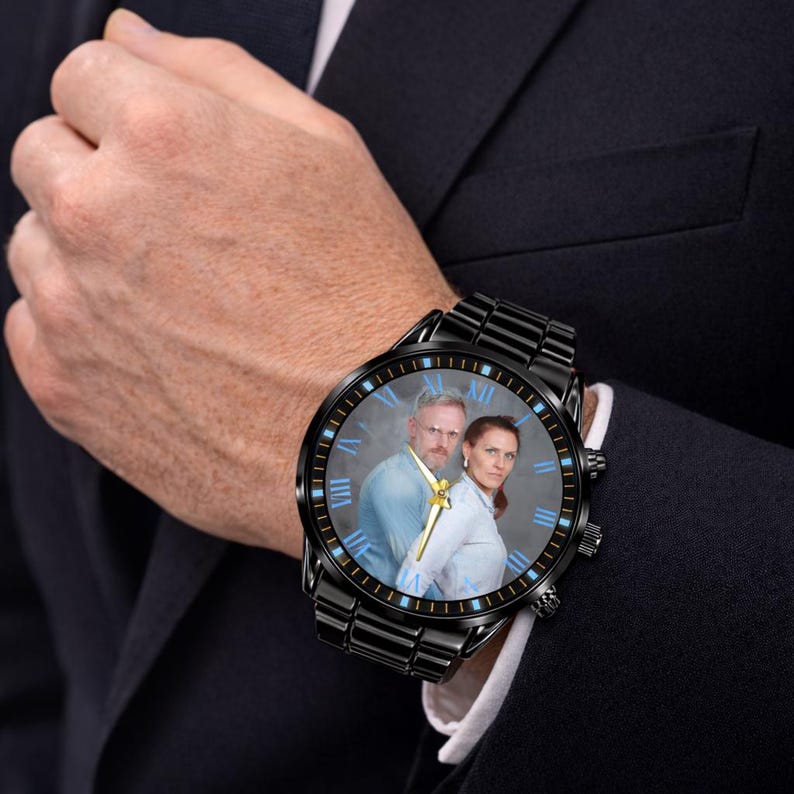 Puede incluir: Reloj de pulsera negro con una foto de una pareja en la esfera. El reloj tiene una correa de metal negro y un bisel negro con n&uacute;meros romanos azules. Las manecillas del reloj son doradas.