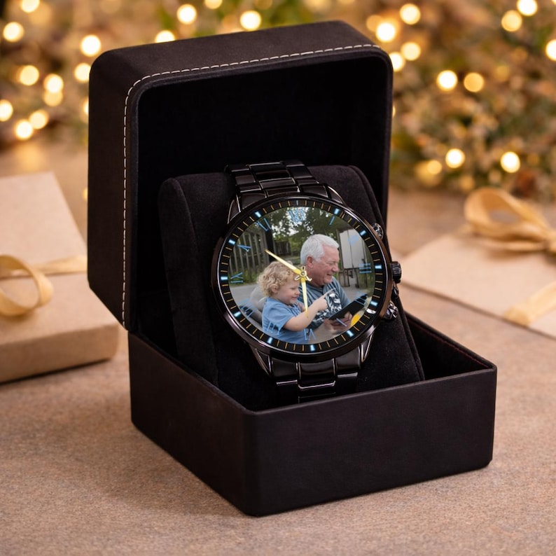 May include: Black wristwatch with a photo of a man and a child on the watch face, presented in a black gift box. The watch has a black metal band and a gold-colored watch hand. The box is open, revealing the watch on a black pillow.
