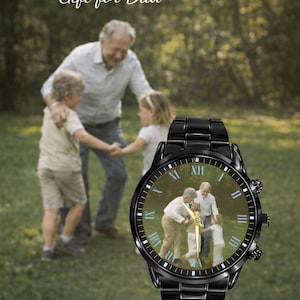May include: Black wristwatch with a photo of a family. The watch has a black metal band and a round face with Roman numerals. The background shows a family playing in a park. Text on the image reads "Gift for Family, Gift for Dad."