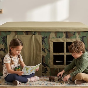 Könnte beinhalten: Ein rechteckiges Spielzelt mit Tarnmuster, einem einfarbigen olivgrünen Dach, einer Stofftür und einem quadratischen Fenster mit kreuzförmigem Rahmen. Das Zelt hat ein strukturiertes Design mit dunkelgrünen, braunen und beigen Mustern.