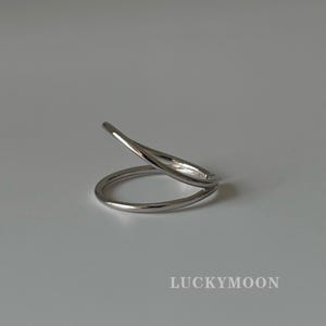 以下が含まれることがあります： 滑らかで光沢のある仕上げのシルバー調のリング。重なり合うオープンなデザインが、しずく型の隙間を作り出しています。画像右下には、すっきりとしたサンセリフ体のフォントで「LUCKYMOON」という文字が印字されています。
