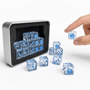 Könnte beinhalten: Ein Set aus transparenten sechsseitigen Acrylwürfeln mit blauen Punkten und einem blauen kreisförmigen Symbol auf einer Seite. Mehrere Würfel befinden sich in einer rechteckigen silbernen Metalldose mit schwarzer Schaumstoffeinlage.