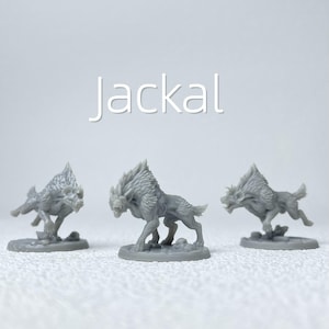 Può includere: Tre figurine di sciacallo grigie sono esposte su sfondo bianco. La parola "Jackal" è scritta in bianco in alto. Ogni statuetta è scolpita in una posa dinamica, con dettagli di pelliccia e tratti.