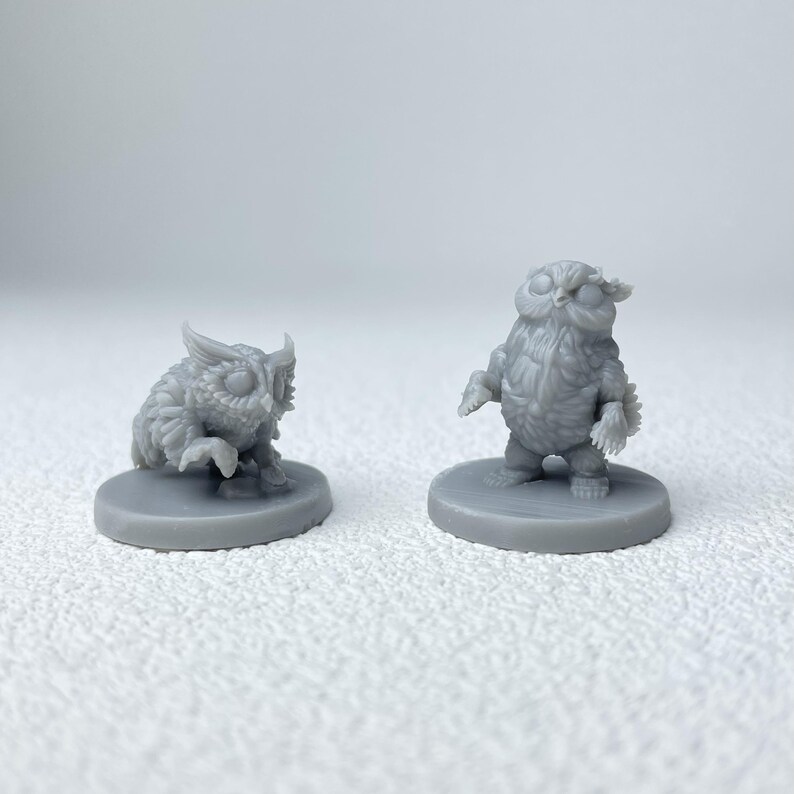 Puede incluir: Dos figuras de b&uacute;ho grises. Un b&uacute;ho est&aacute; agachado, el otro est&aacute; de pie. Ambos est&aacute;n sobre bases circulares. Las figuras tienen texturas de plumas detalladas y ojos grandes, lo que les da una apariencia caprichosa. Probablemente sean miniaturas para juegos de mesa o art&iacute;culos decorativos.