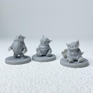 Puede incluir: Tres figuras de b&uacute;hos grises en diferentes poses. Un b&uacute;ho est&aacute; de pie, otro sentado y el tercero sale de un huevo. Cada figura est&aacute; sobre una base circular, mostrando texturas detalladas de plumas.