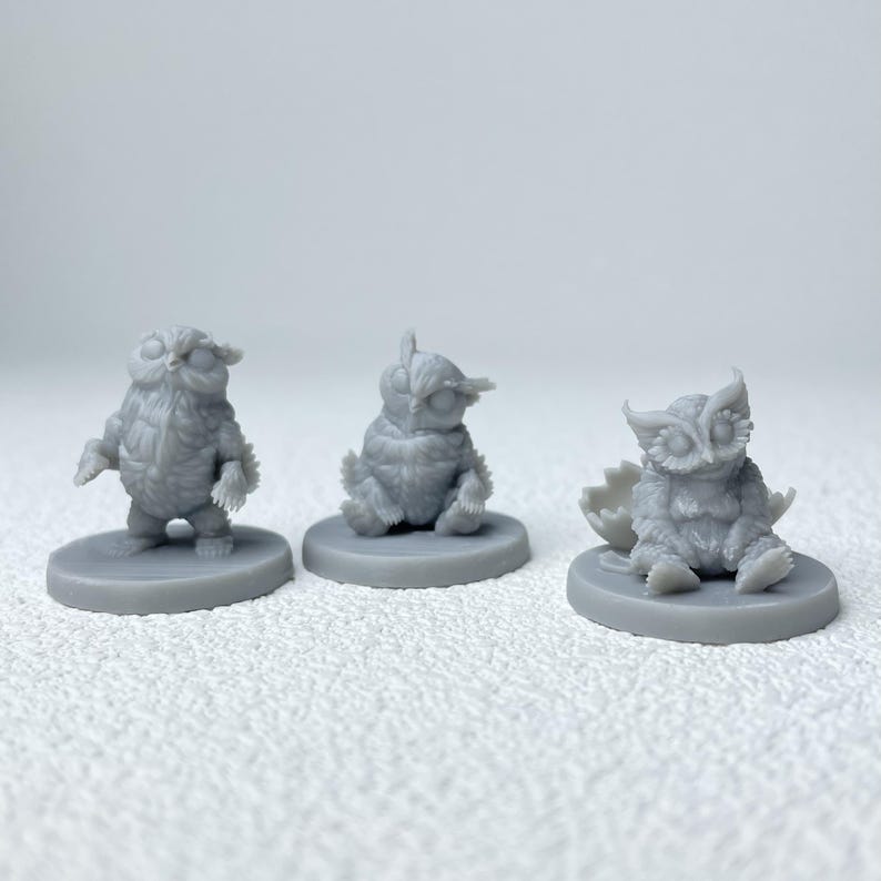 Puede incluir: Tres figuras de b&uacute;hos grises en diferentes poses. Un b&uacute;ho est&aacute; de pie, otro sentado y el tercero sale de un huevo. Cada figura est&aacute; sobre una base circular, mostrando texturas detalladas de plumas.