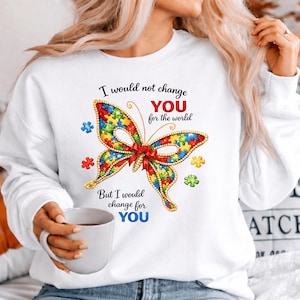 May include: White sweatshirt featuring a colorful butterfly design made of puzzle pieces. The butterfly has a red bow and is surrounded by puzzle piece accents. Text on the shirt reads, "I would not change YOU for the world, But I would change for YOU."