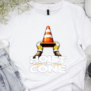 May include: White t-shirt featuring a graphic of a traffic cone held by gloved hands, with the text "HOIST THE CONE" in a bold, stylized font. The cone is orange and white, and the gloves are yellow.