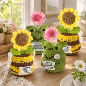 May include: Four crocheted figures including two yellow and brown striped bees with sunflowers and two green frogs with pink flowers. Each figure holds a small white sign with printed text messages like Thank you for bee-ing and Never frog-et.