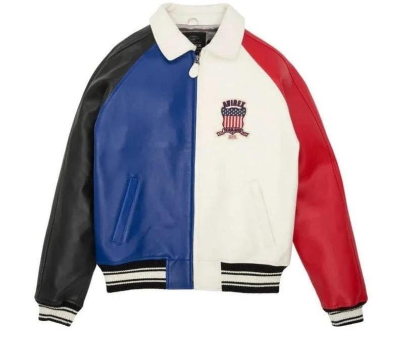 May include: A color-blocked jacket featuring a white collar, a black sleeve, a blue front panel, a white front panel, and a red sleeve. The jacket has a front zipper closure, striped ribbed cuffs and hem, and an Avirex shield patch on the chest.