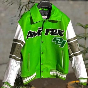 May include: A bright green varsity jacket featuring white and olive green sleeves with striped ribbed cuffs. The front displays the text Avi rex in black lettering with a white outline, alongside a green and white number 24 patch on the chest.
