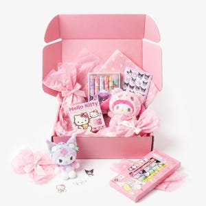 May include: A pink gift box filled with Hello Kitty themed items. The box contains a plush toy, a notebook, a set of crayons, and other accessories. The box is surrounded by pink tissue paper and bows. A second box of crayons is also visible.