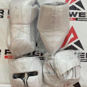 Puede incluir: Un conjunto de equipo de boxeo blanco, que incluye guantes, protector de cabeza y protector inguinal, todo empaquetado en plástico transparente. Cada artículo presenta el logotipo "FLY".
